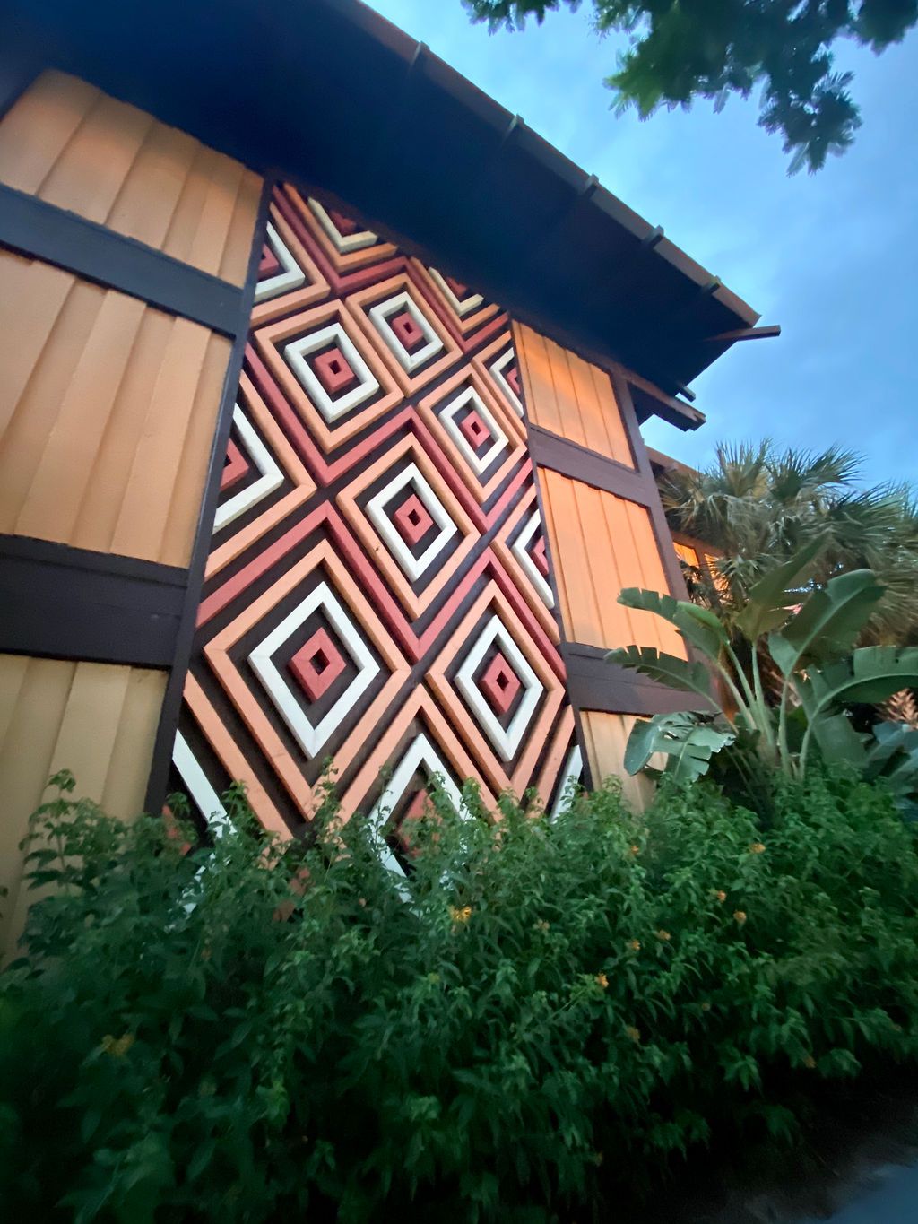A wooden building with geometric red and white diamond patterns on its facade surrounded by lush greenery.