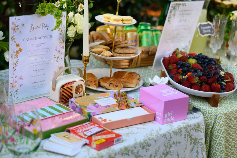 Elegant tea party setup with menu, pastries, berries and pink decor boxes on a lace tablecloth.