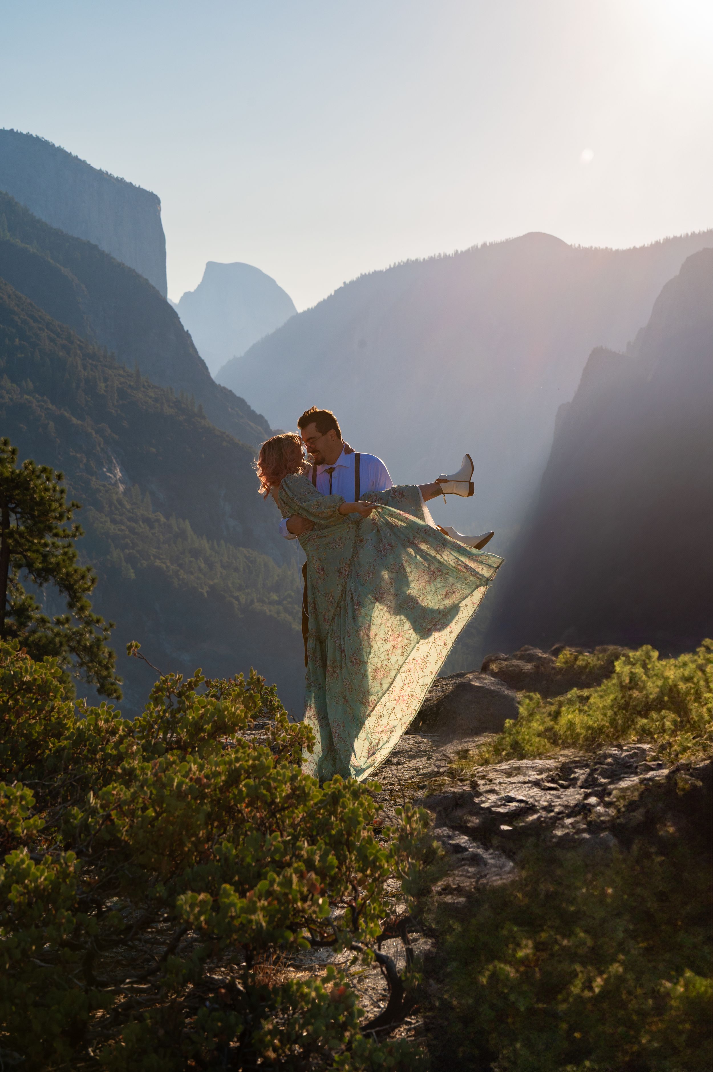 A romantic couple poses dramatically against the majestic backdrop of Yosemite Valley mountains at sunset.