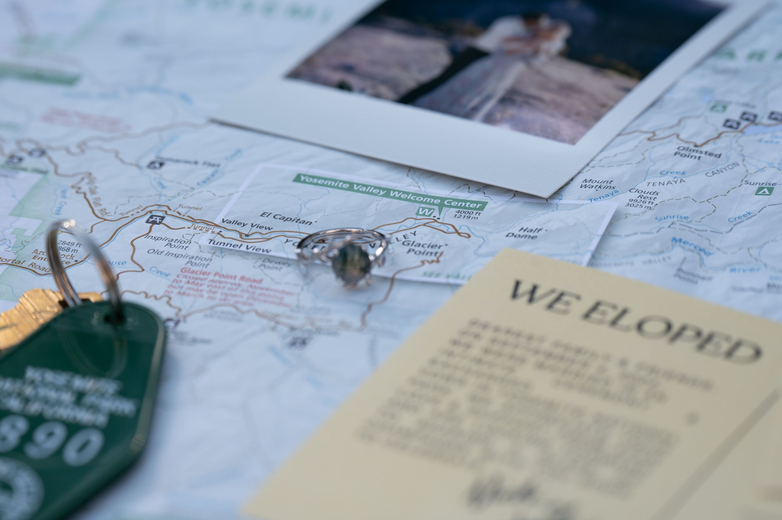 Travel planning items including a map, polaroid photo, and vintage room key tag laid out on a surface.