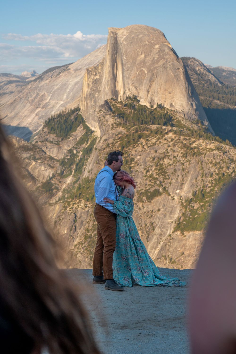 A couple embraces at Glacier Point with Half Dome rock formation in Yosemite National Park at sunset.