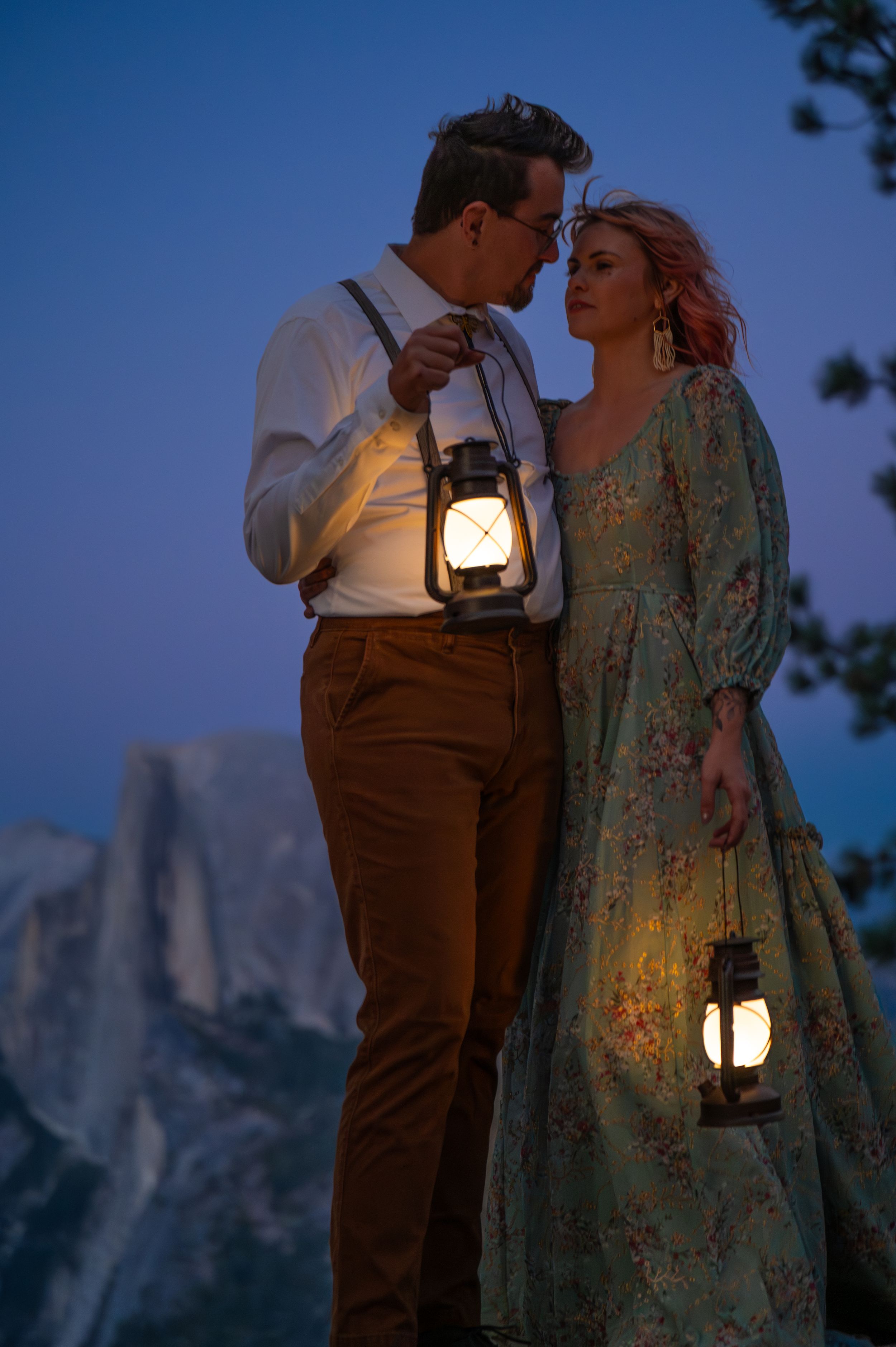 A romantic evening scene with lantern light against mountain backdrop as couple shares intimate twilight moment.