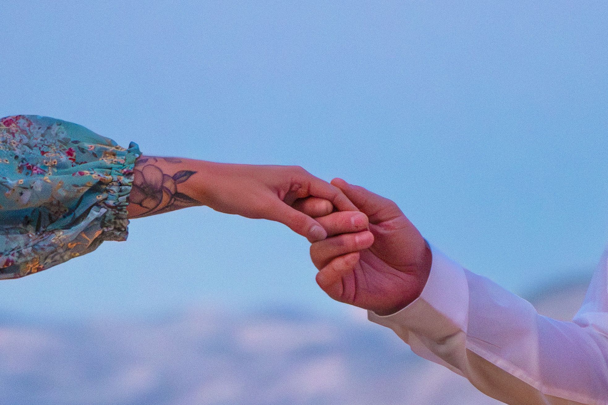 Two hands reach out to hold each other against a dreamy blue sky background.