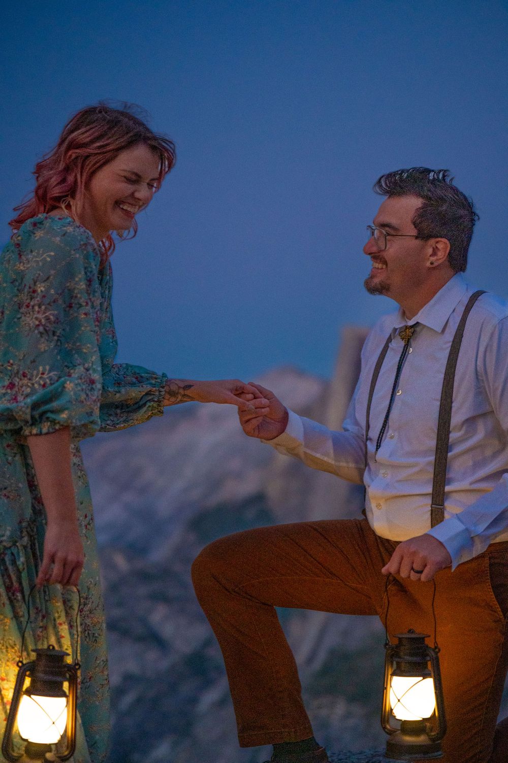 A couple shares a romantic moment at dusk with lanterns glowing against a mountain backdrop.