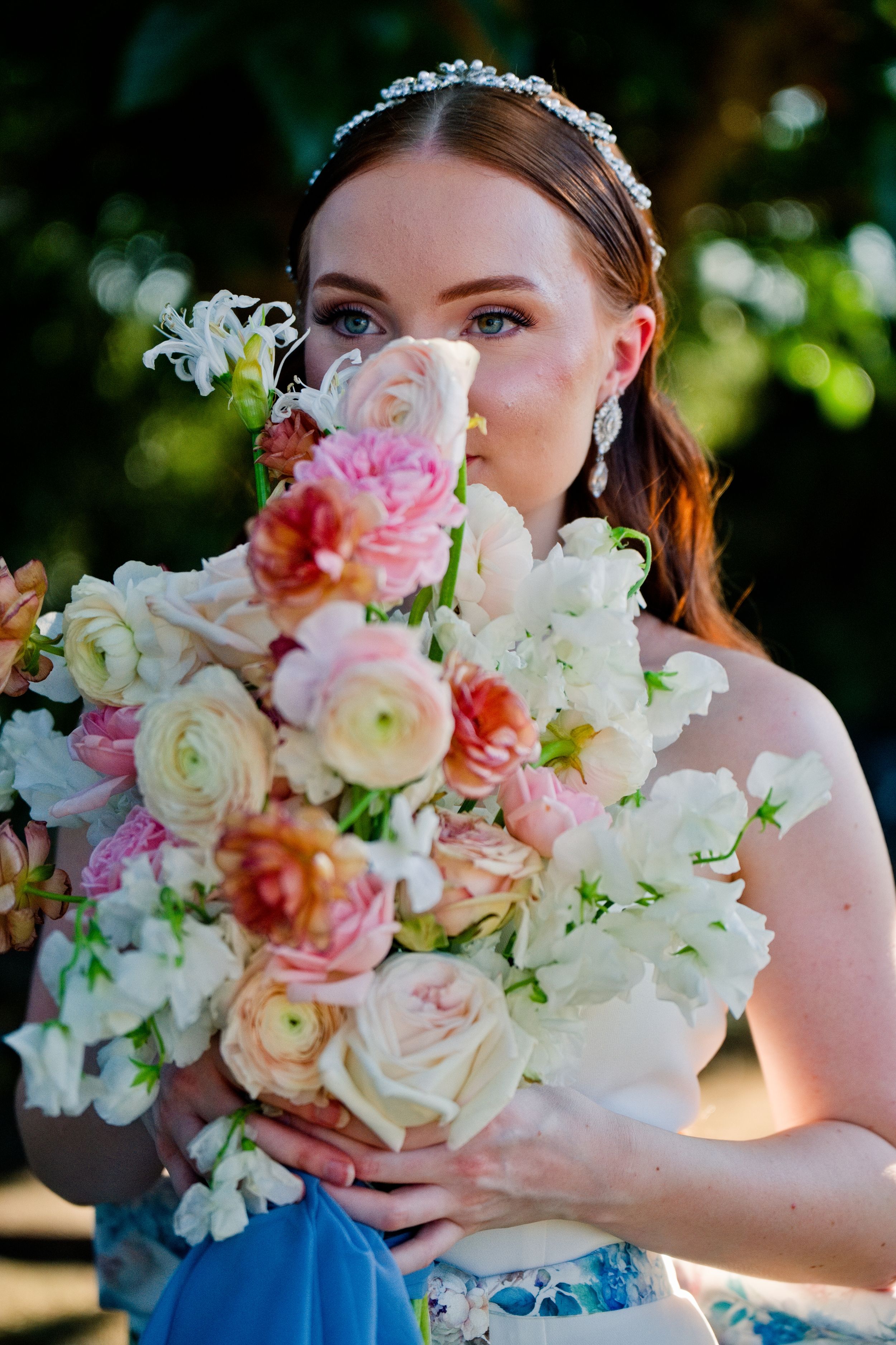 A blooming bridal bouquet featuring pink and white roses, ranunculus and sweet peas against a blurred garden background.
