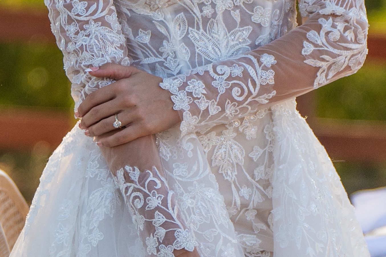 Close-up detail of an ornate lace wedding dress sleeve with an engagement ring visible on the hand.