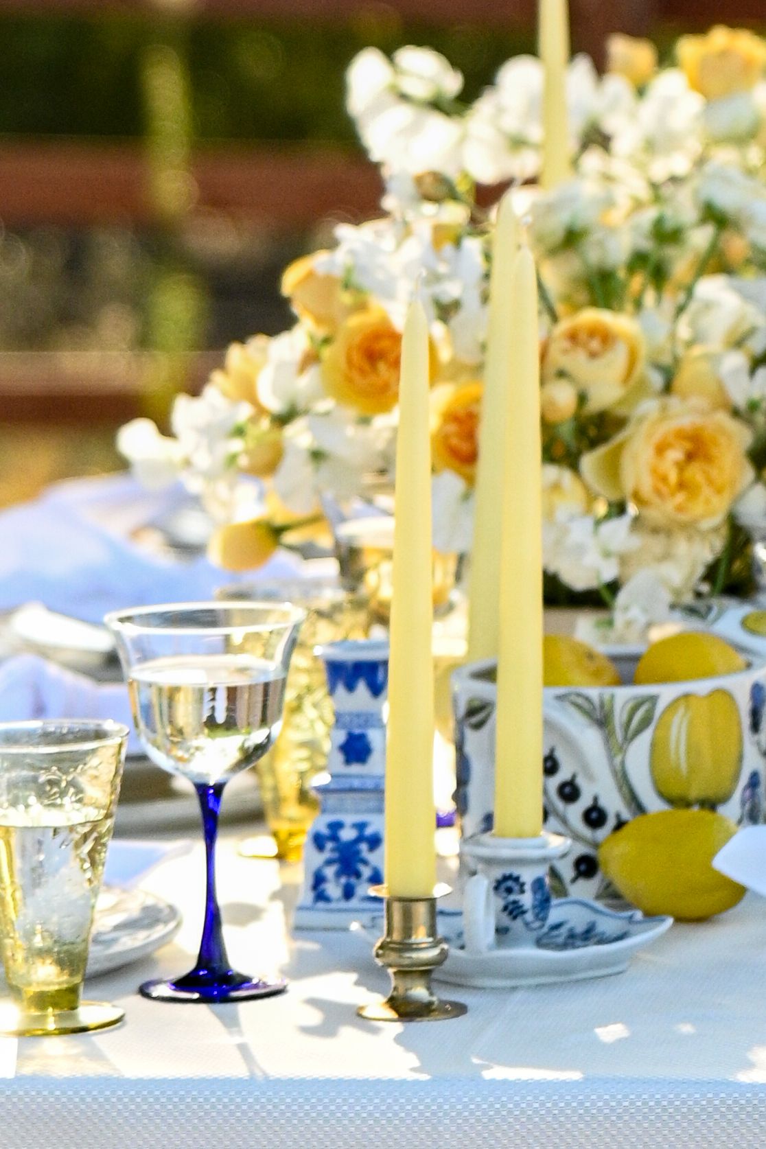 Elegant table setting with yellow roses, blue and white china, cobalt wine glasses and tall yellow taper candles.