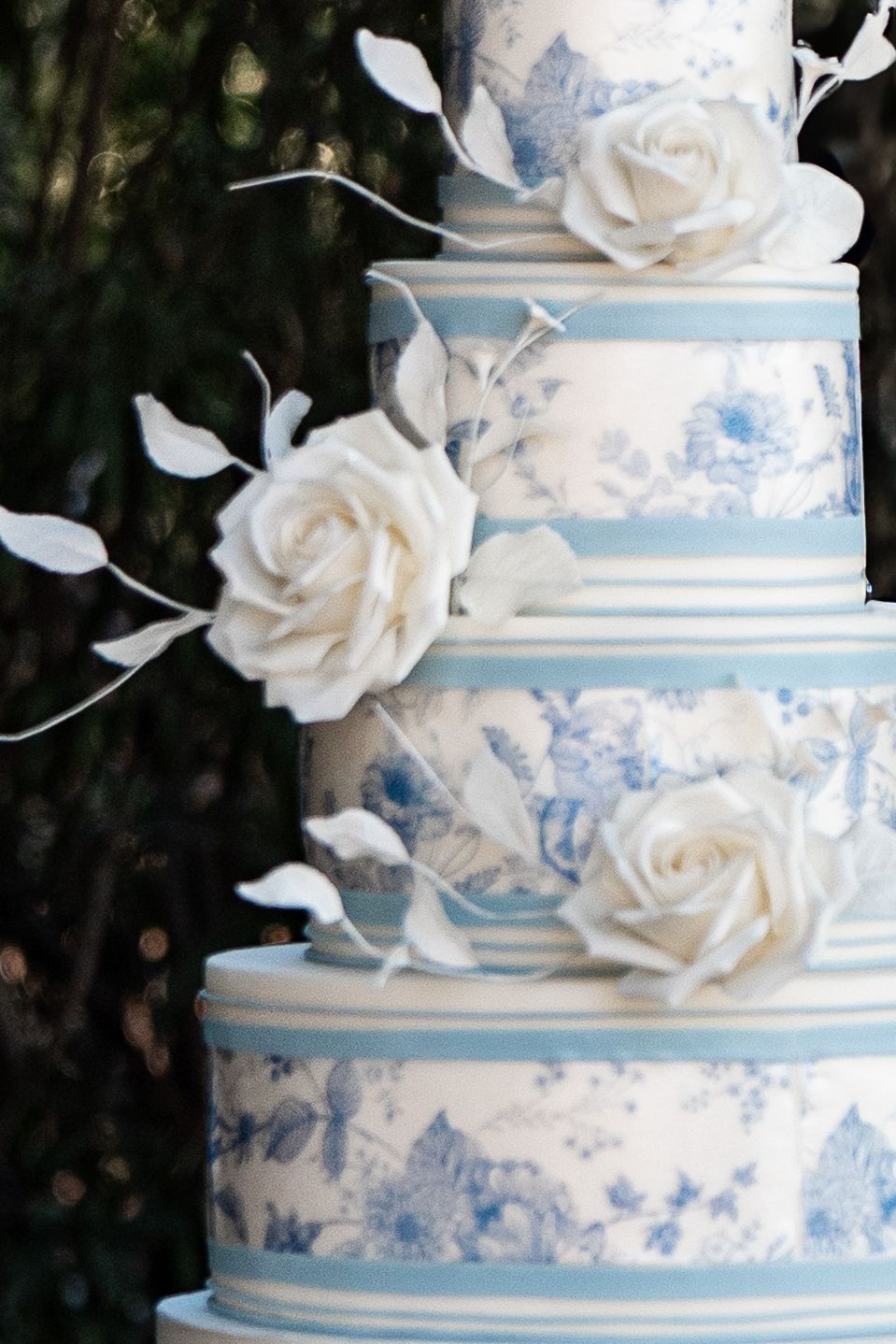 Elegant white and light blue wedding cake with delicate floral pattern and handcrafted white sugar roses as decorations.