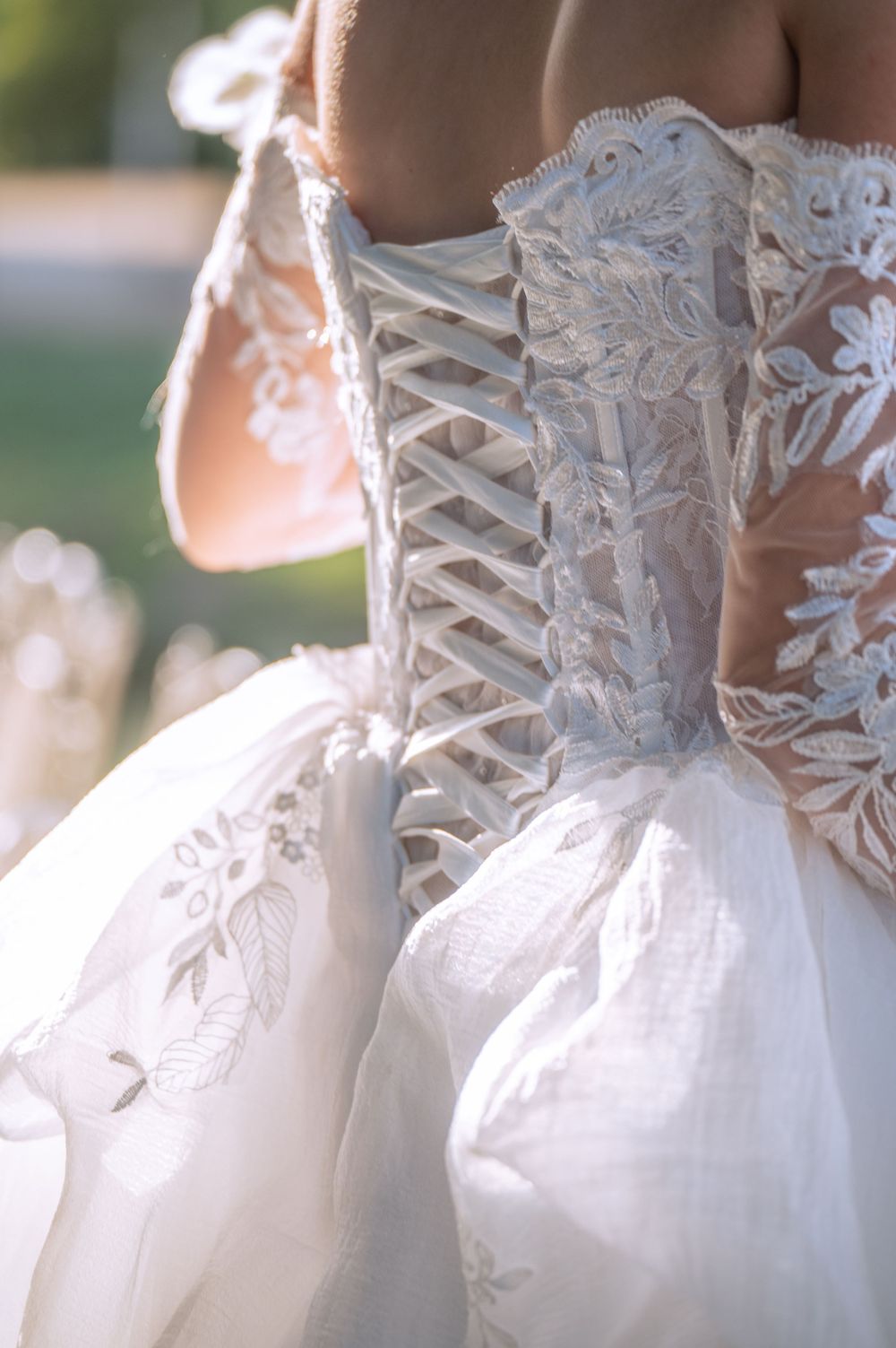 Close-up detail of a white wedding dress showing intricate lace pattern and corset-style back lacing in natural lighting.