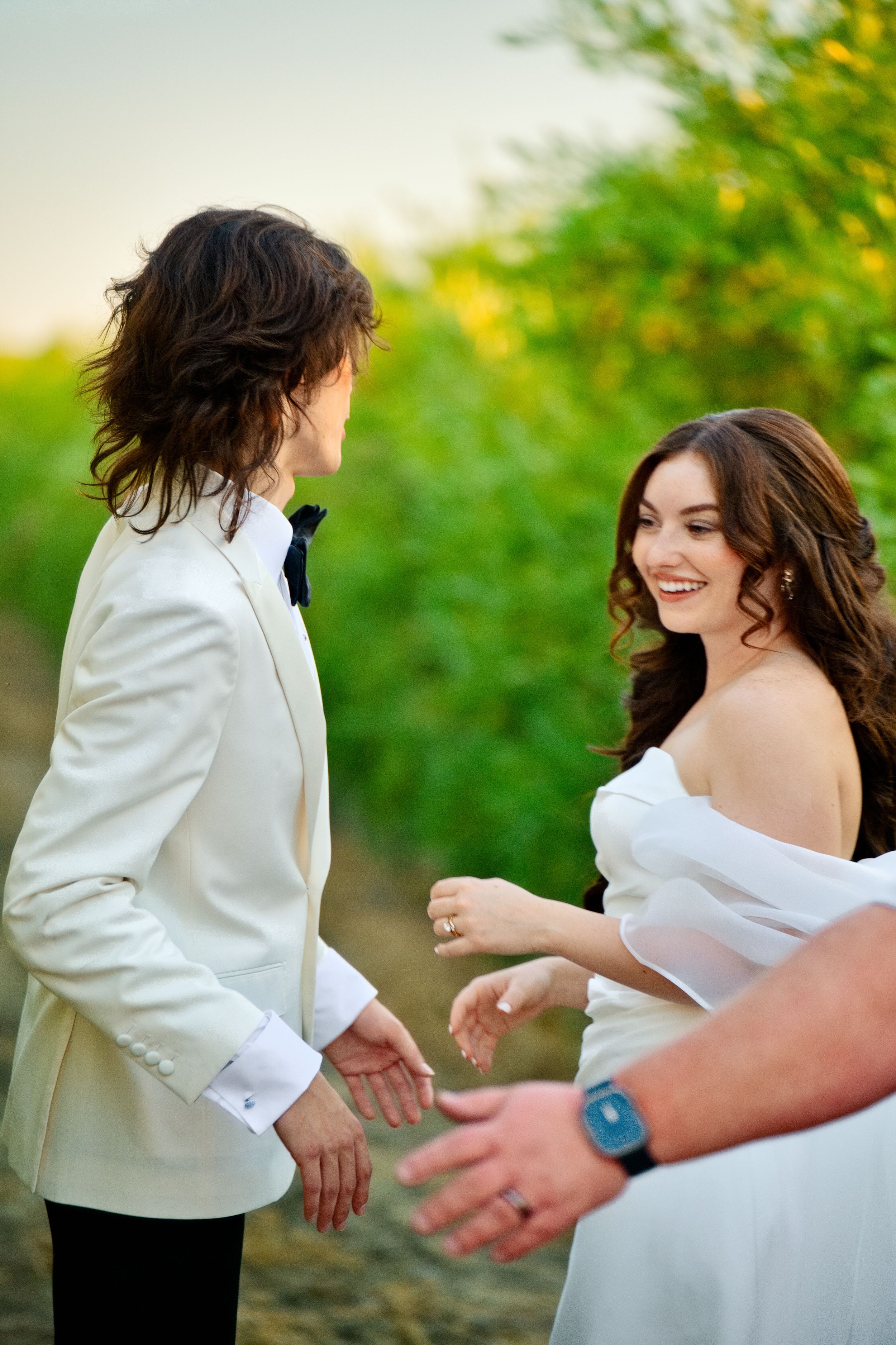 A couple shares a joyous moment at an outdoor wedding ceremony with green foliage in the background.