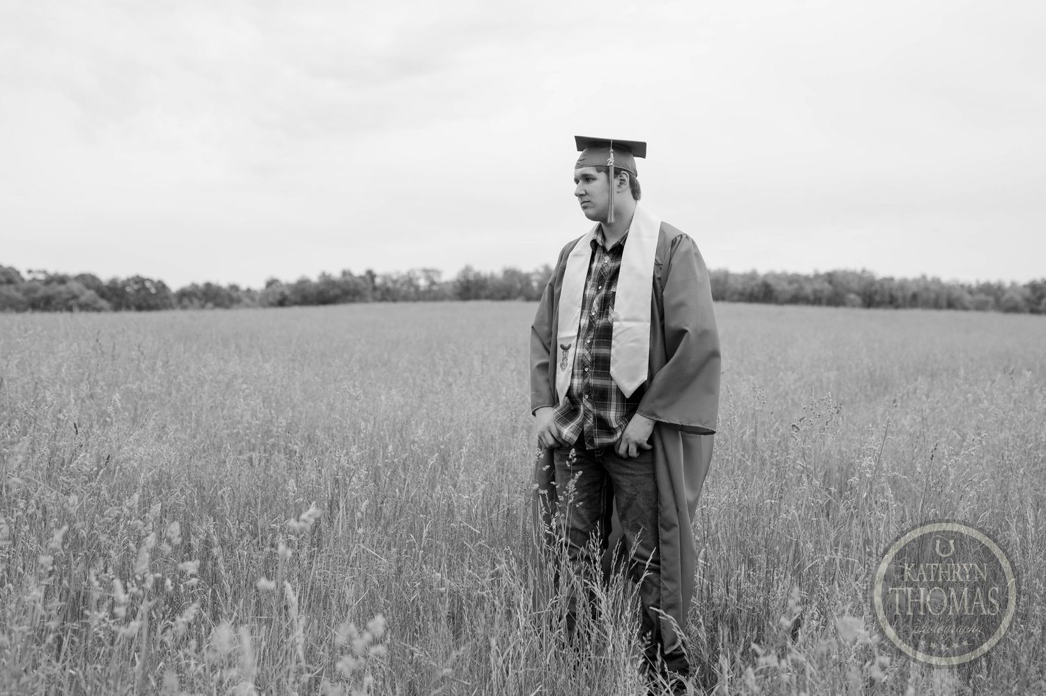 A person stands in a grassy field wearing a jacket and cap while holding what appears to be equipment in black and white.