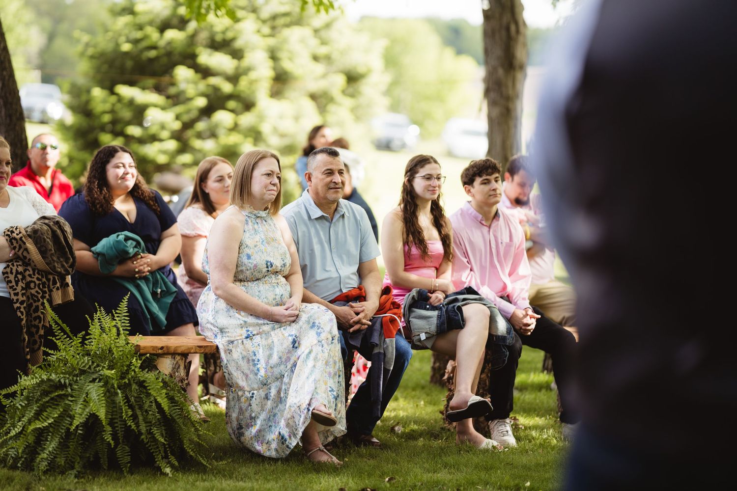 A group of people sitting casually on a grassy hillside under trees during an outdoor gathering.