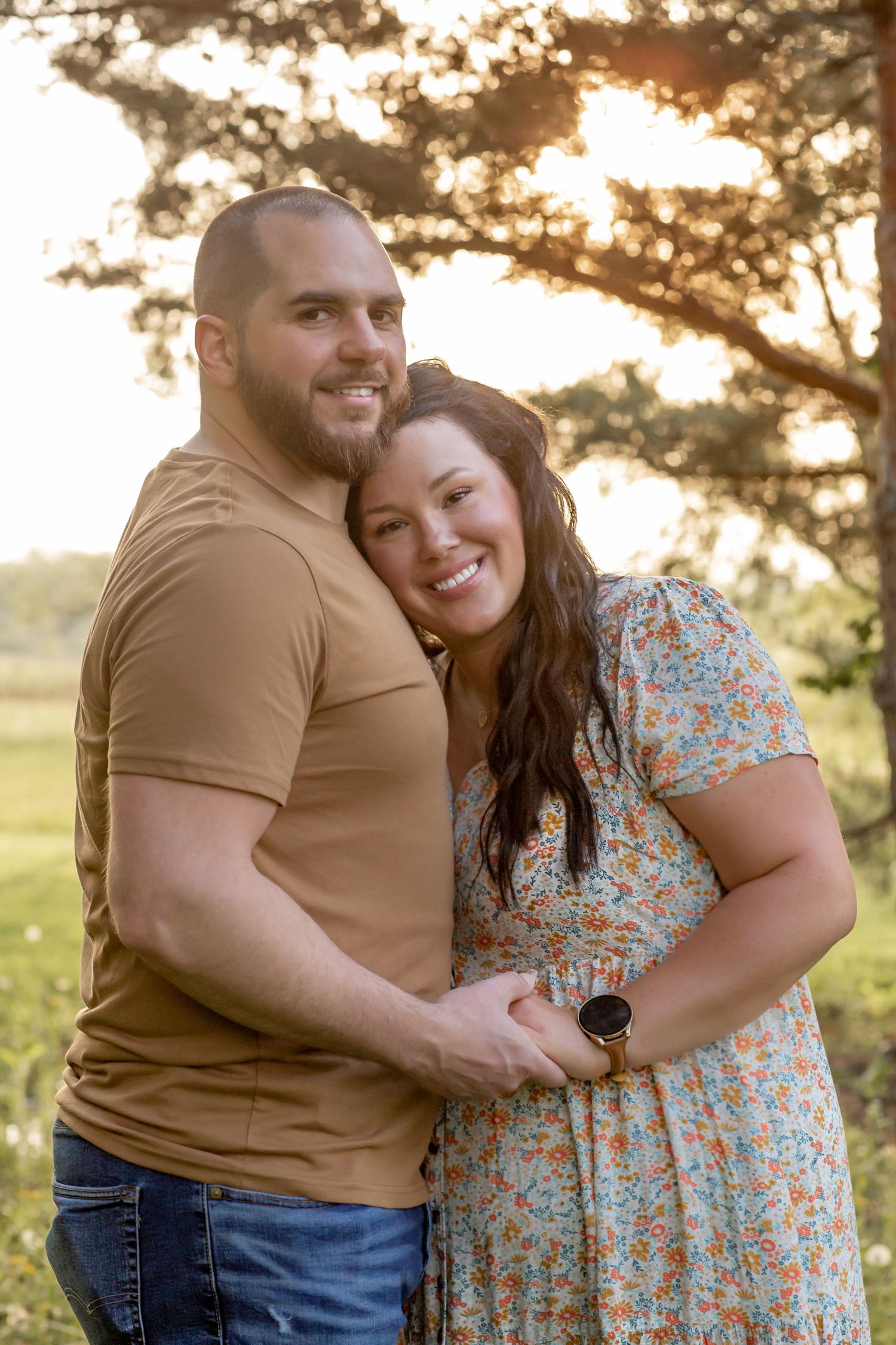 Happy couple embracing at golden hour in a sunlit outdoor field.