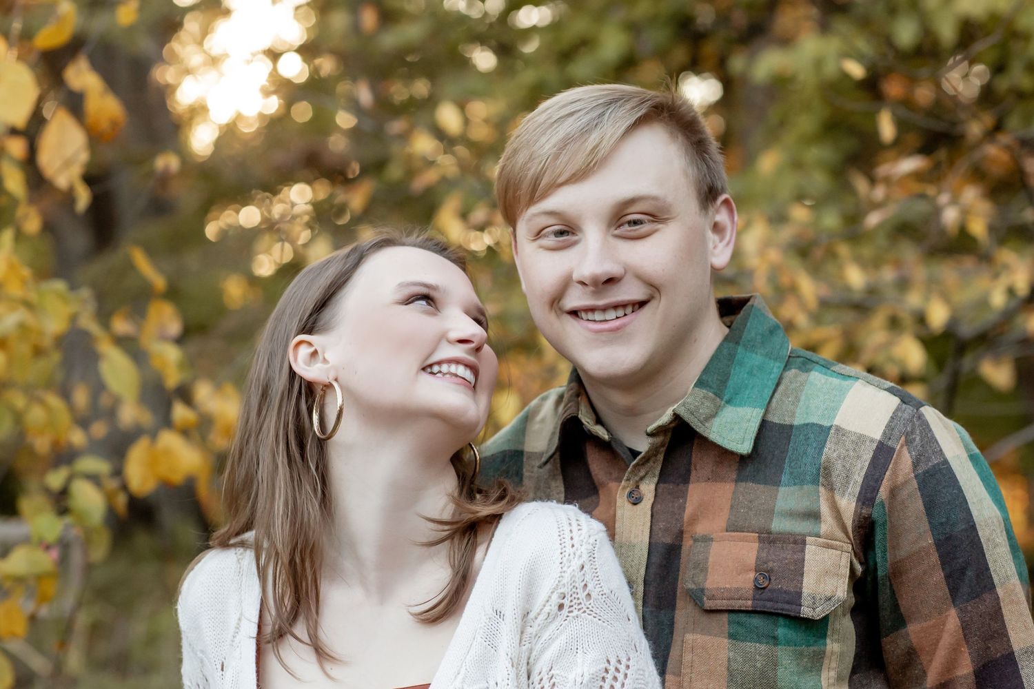 Young smiling couple laughing together outdoors with colorful autumn leaves in the background.