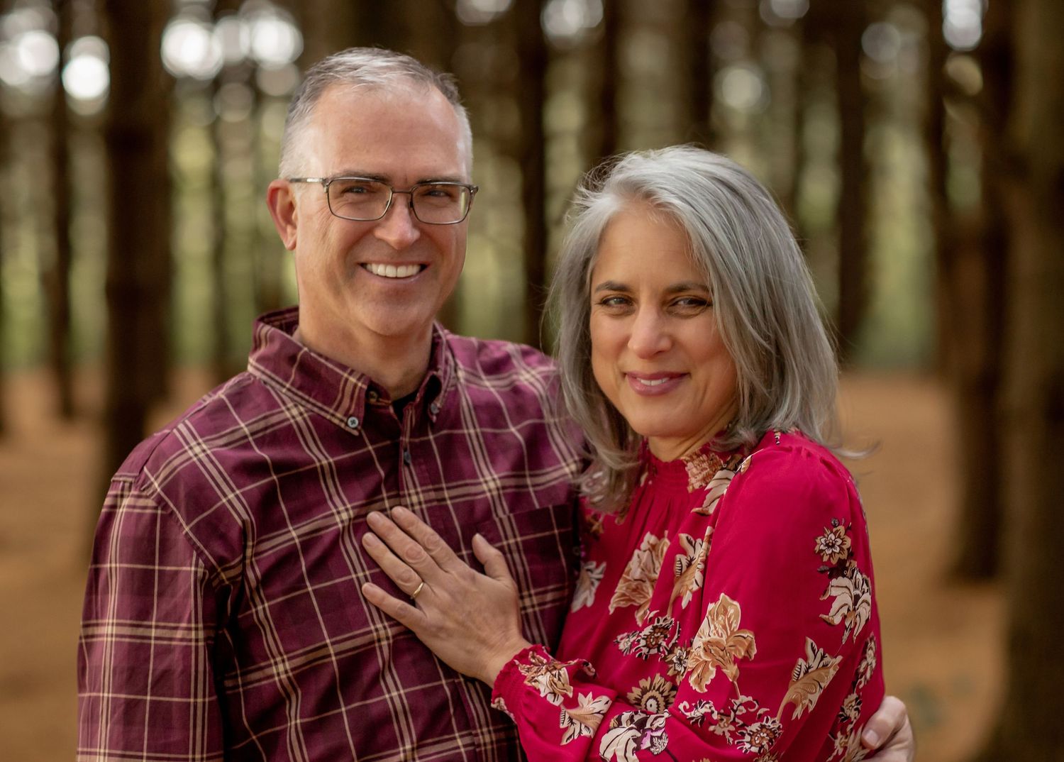 Smiling middle-aged couple posing together in a pine forest setting.