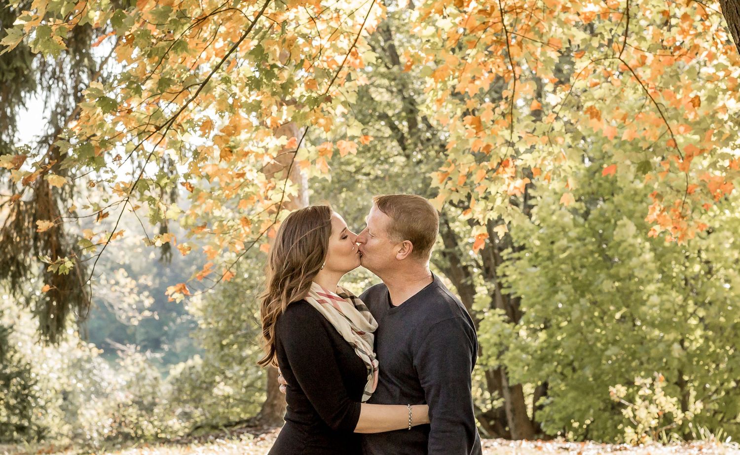 Romantic couple sharing a kiss beneath colorful autumn foliage outdoors.