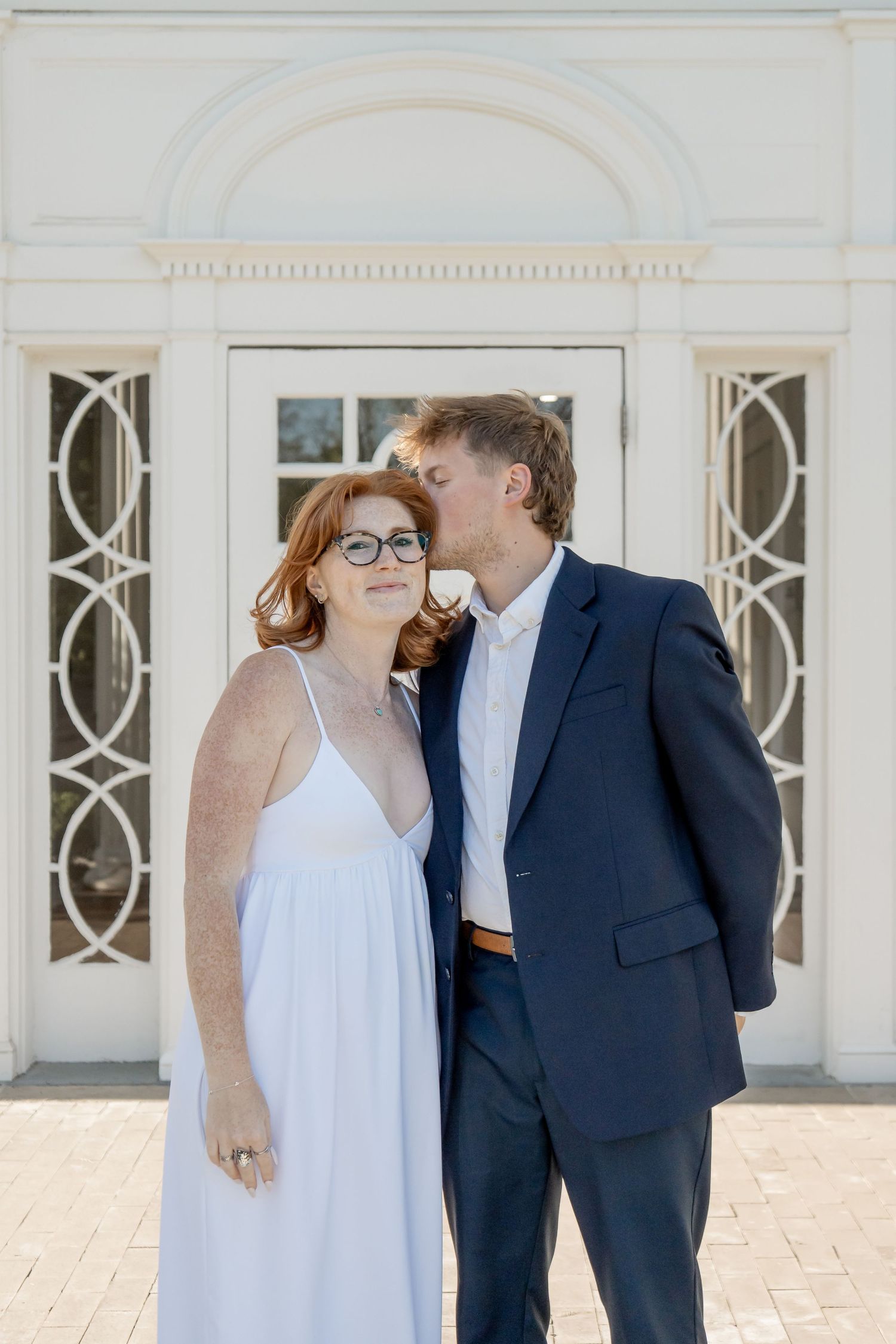 Elegant couple sharing a kiss in front of a white classical building.
