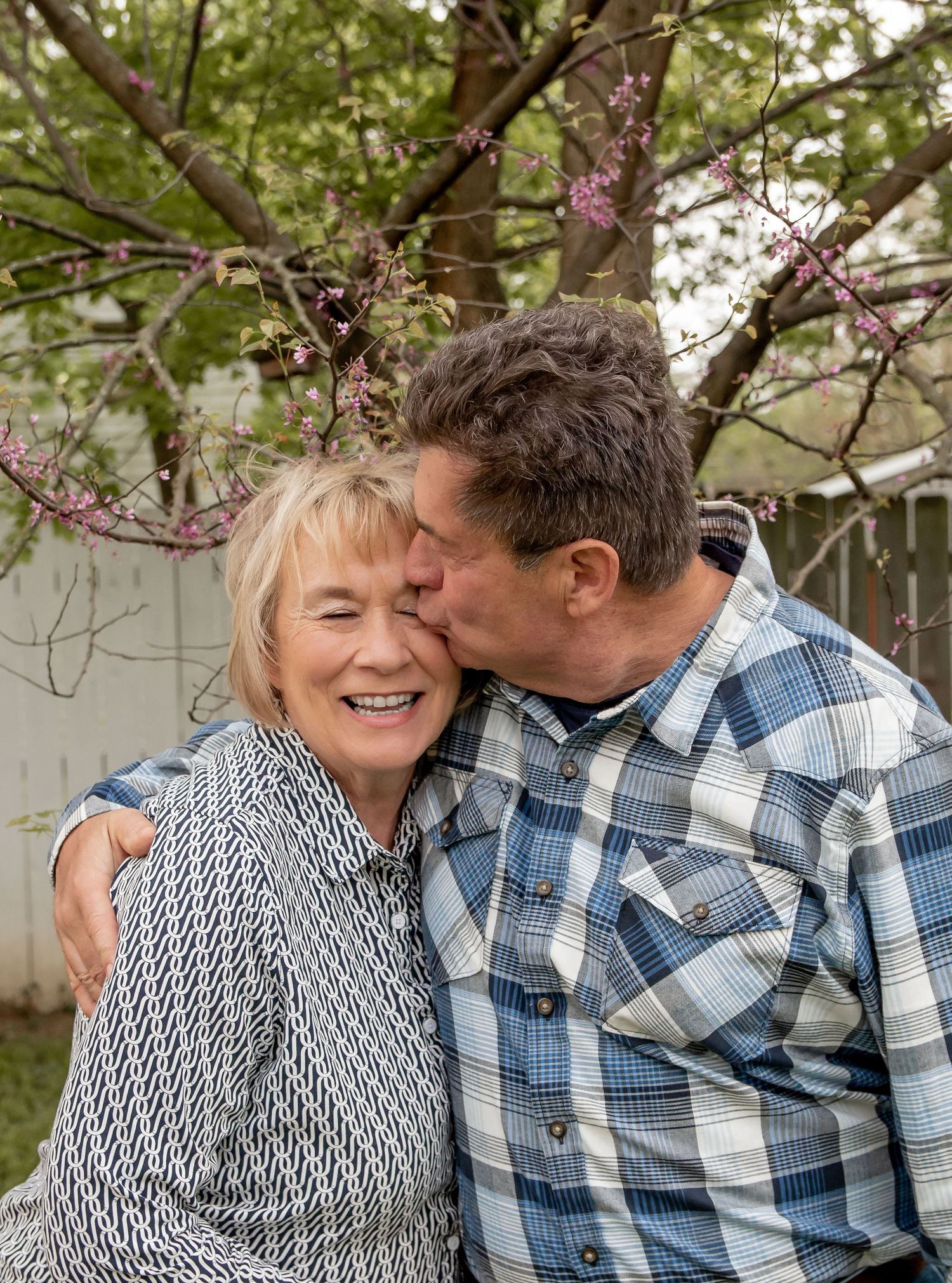 Older couple sharing a tender kiss under blooming spring tree outdoors.