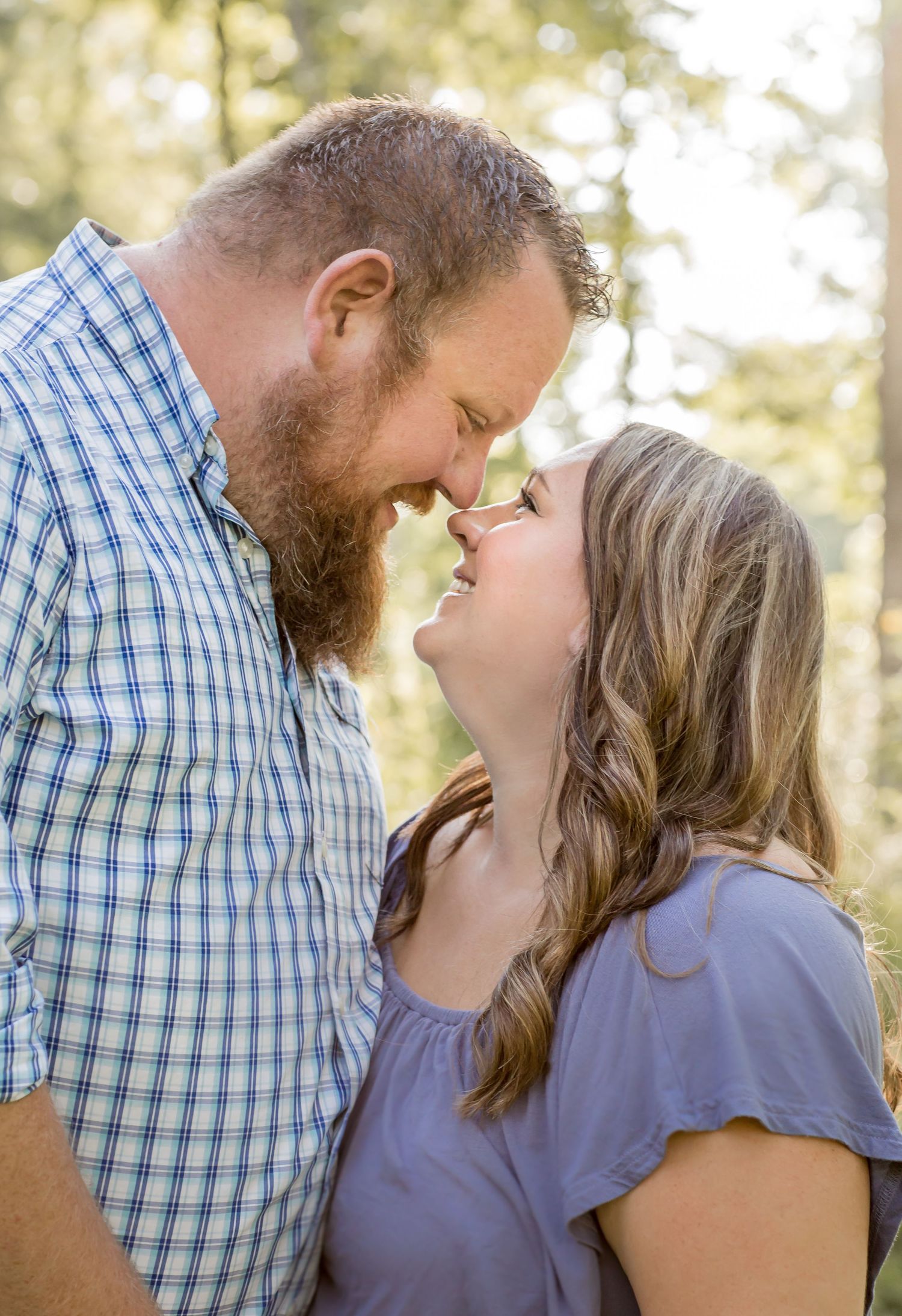 Loving couple sharing an intimate nose-to-nose moment among tall trees.