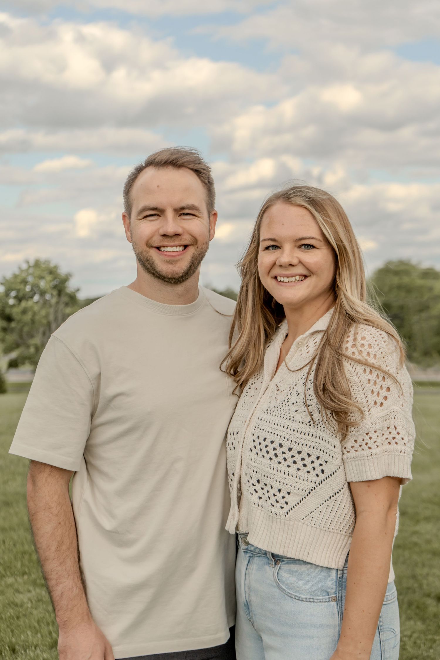 Smiling young couple standing together outdoors under a partly cloudy sky.
