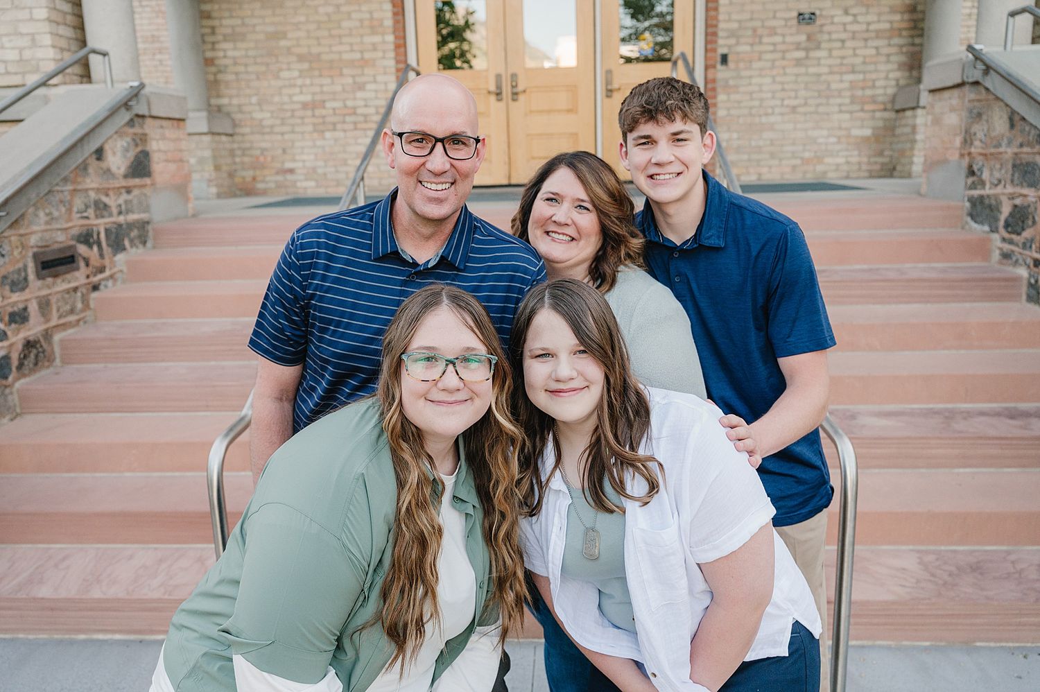 A group of five people sit together smiling on outdoor brick steps for a casual family photo.