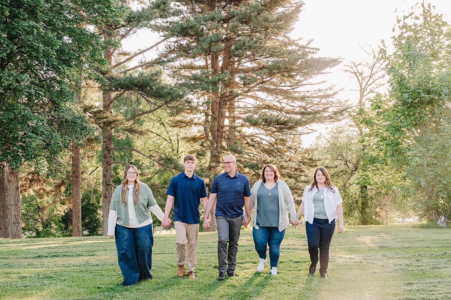 A group walks together through a scenic park with tall pine trees on a sunny afternoon.
