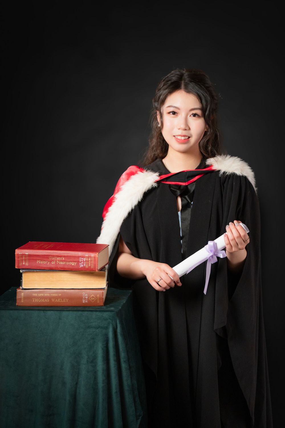 Close-up portrait of a woman in a black graduation gown holding white flowers and books.