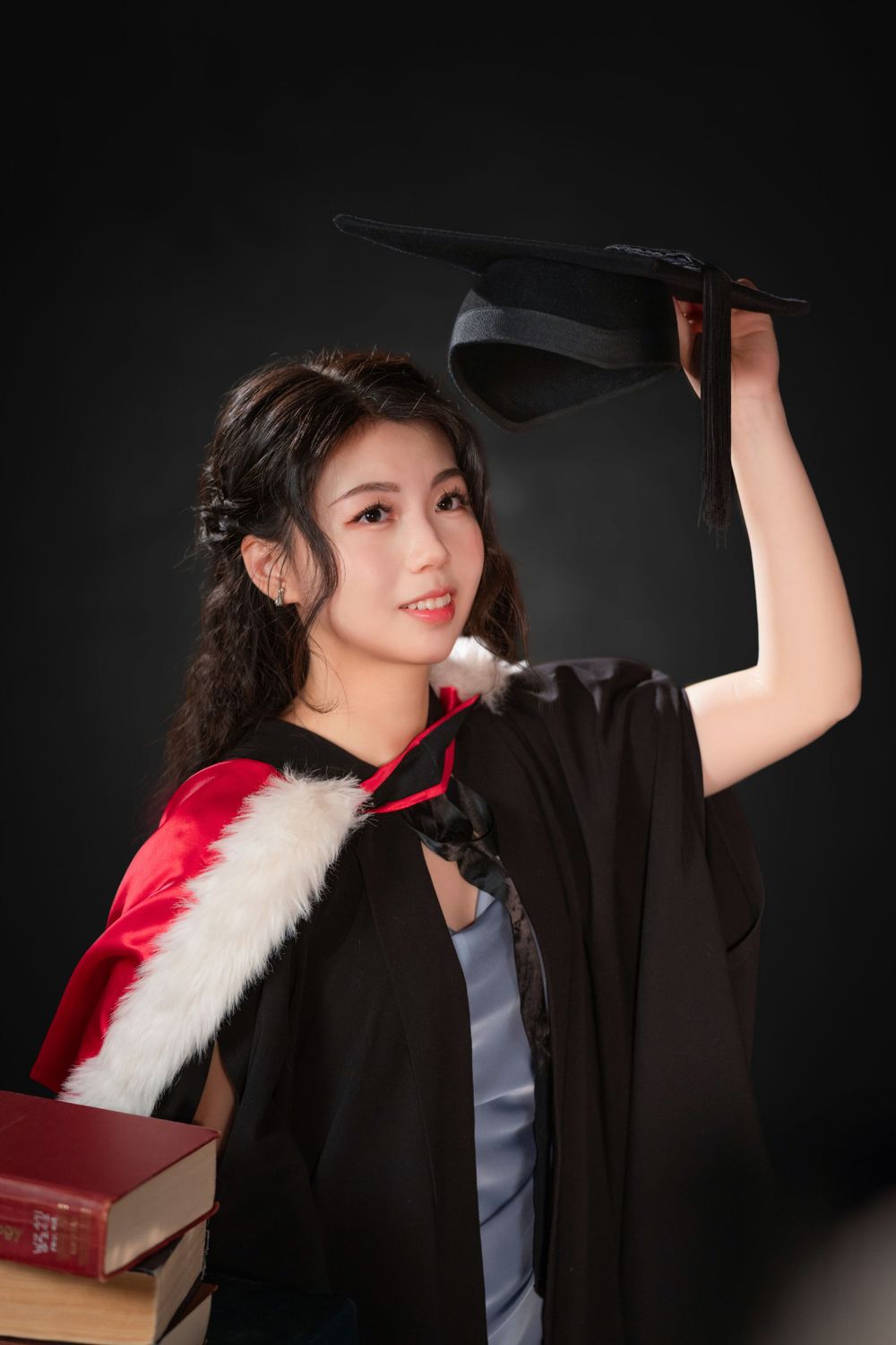 Close-up portrait of a woman in a black graduation gown holding white flowers and books.