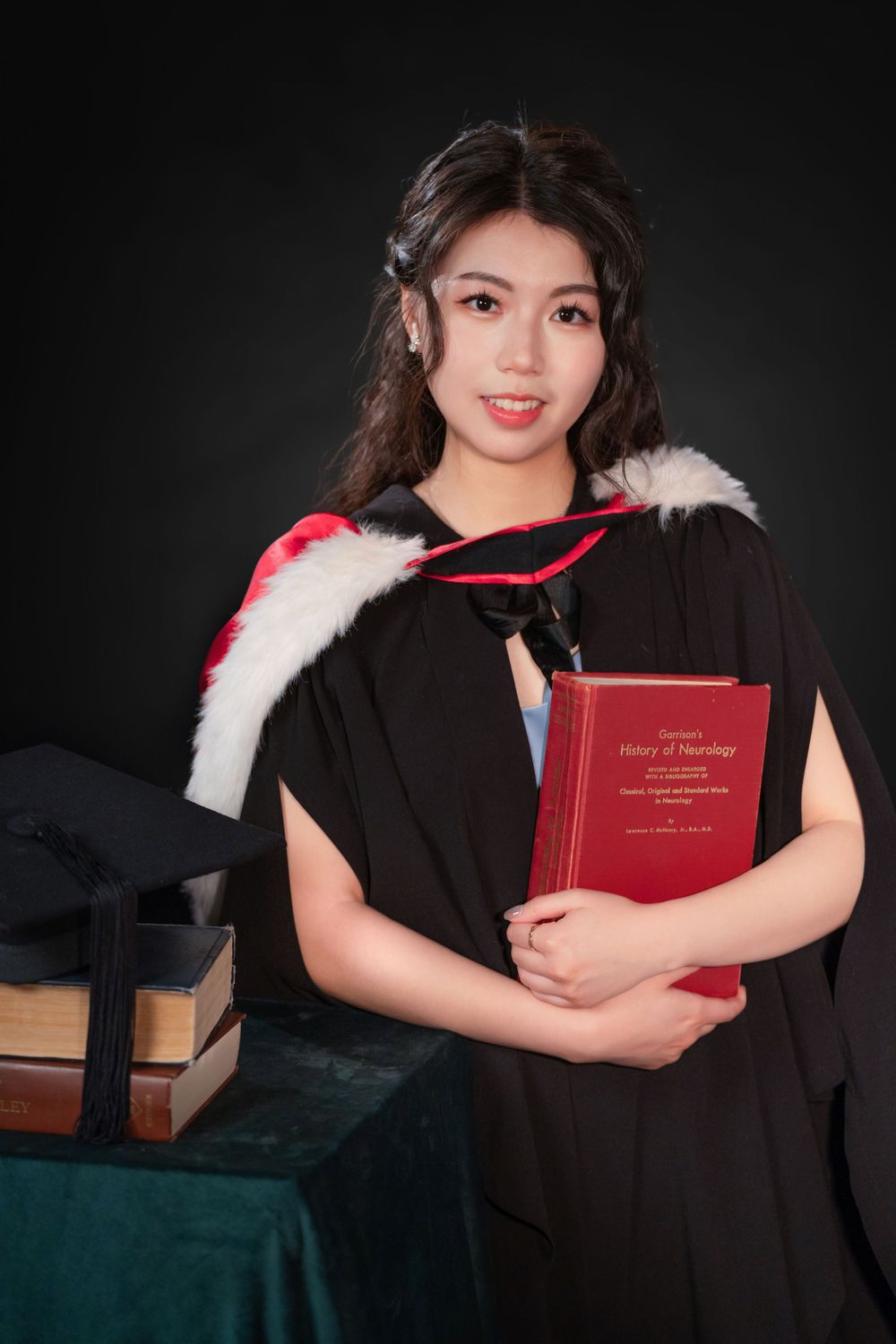 Close-up portrait of a woman in a black graduation gown holding white flowers and books.