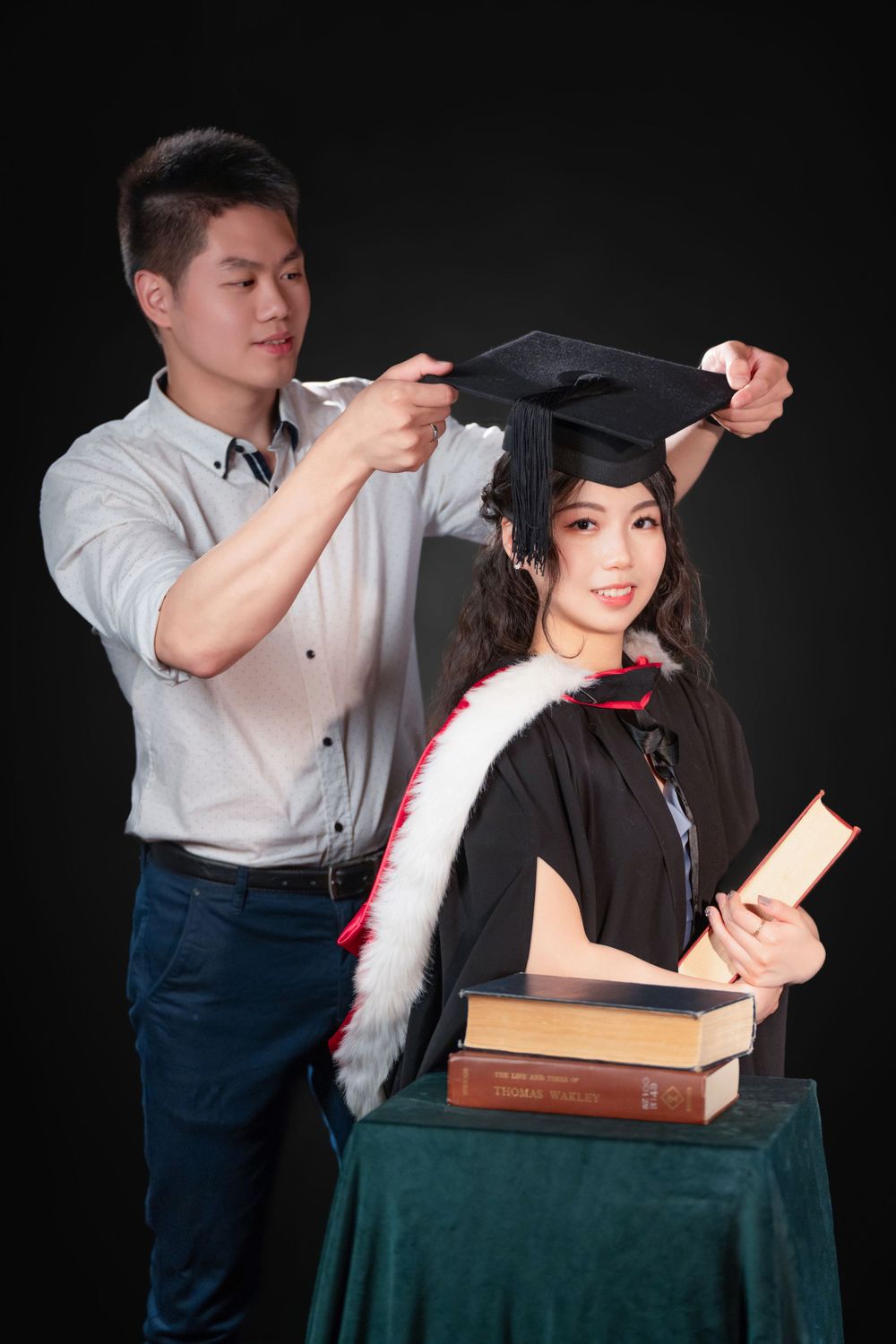 Close-up portrait of a woman in a black graduation gown holding white flowers and books.