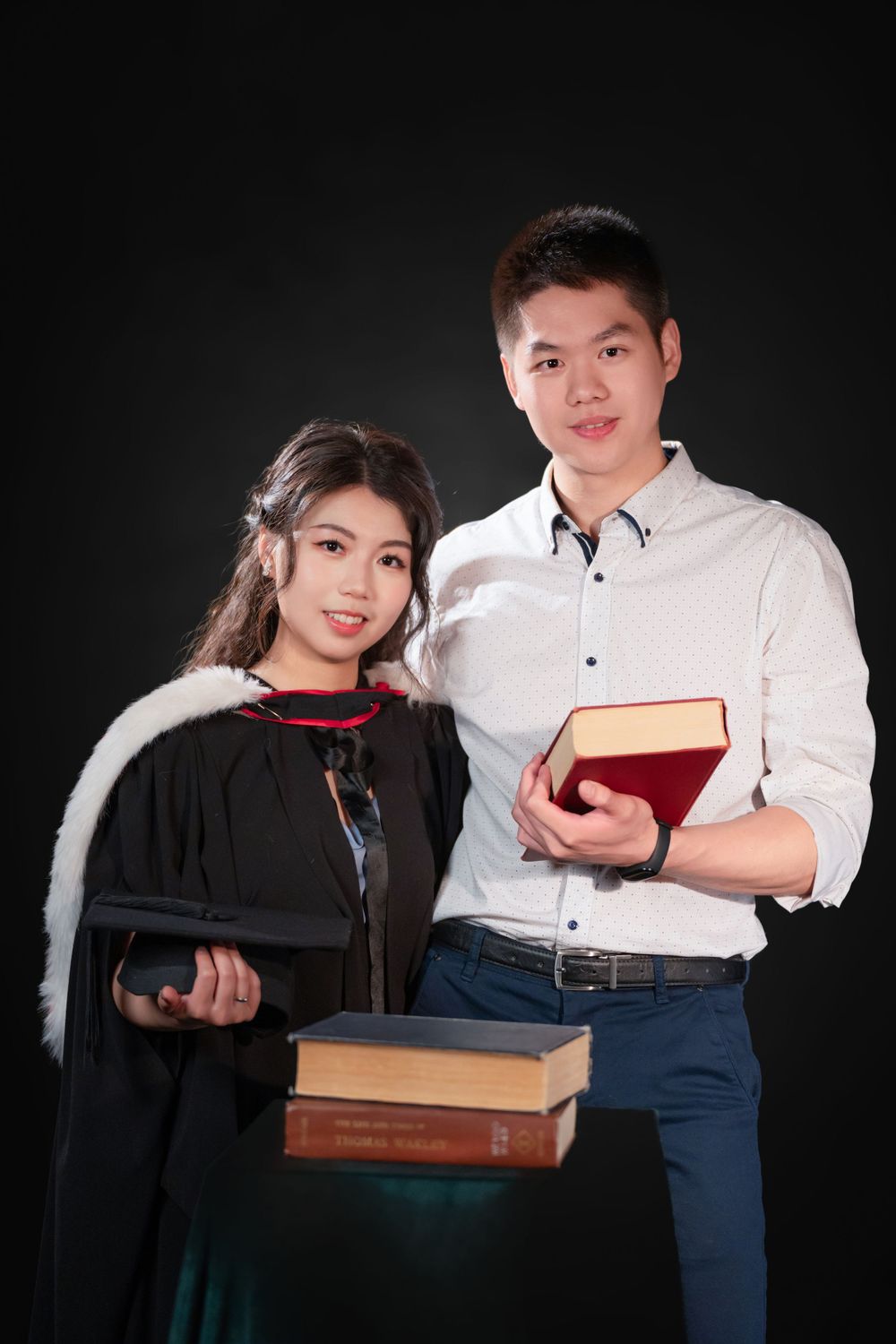 Close-up portrait of a woman in a black graduation gown holding white flowers and books.