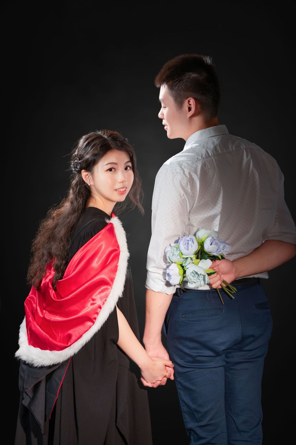 Close-up portrait of a woman in a black graduation gown holding white flowers and books.