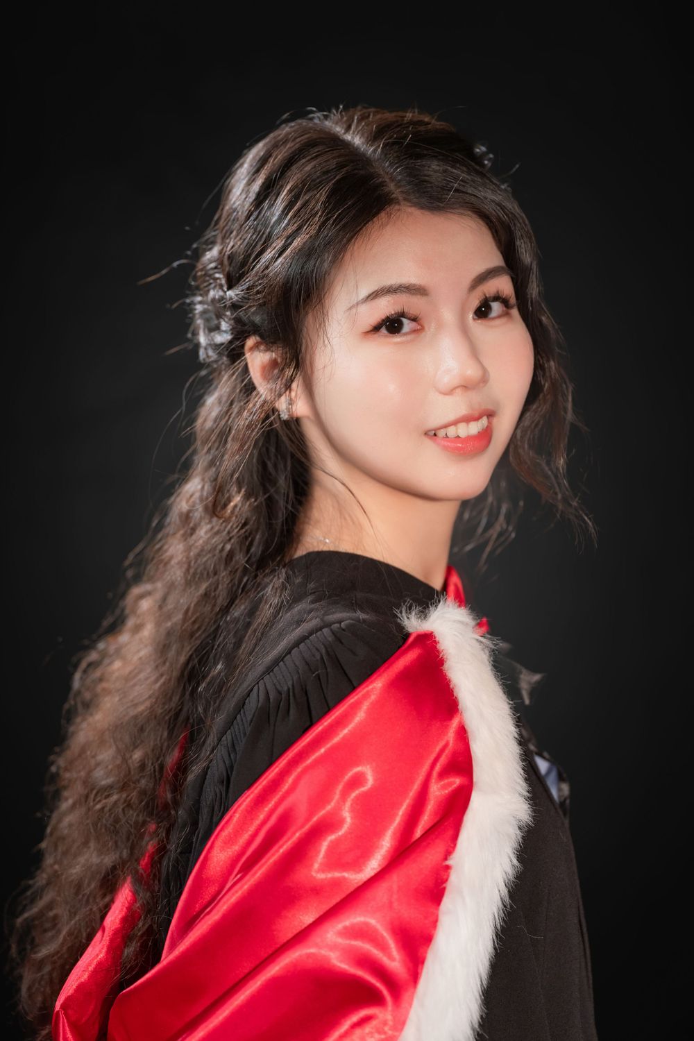 Close-up portrait of a woman in a black graduation gown holding white flowers and books.
