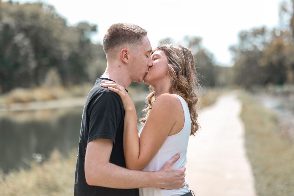 A romantic couple shares an intimate kiss on a pathway near a serene lake during an autumn photo session.