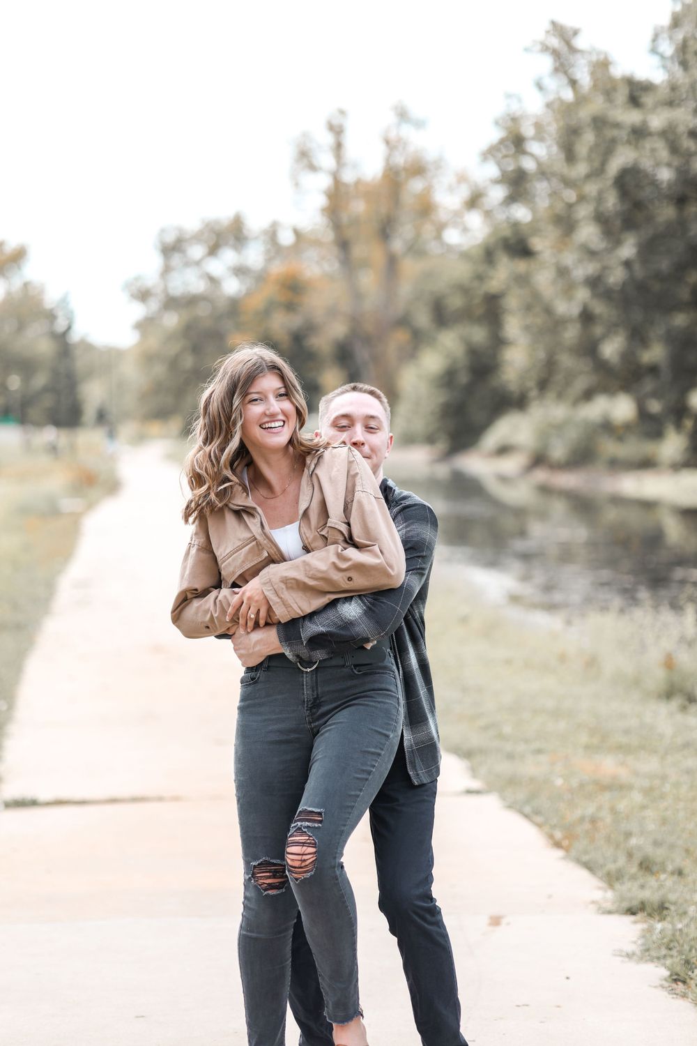 Happy couple laughs together during a casual autumn photoshoot by a lakeside path.