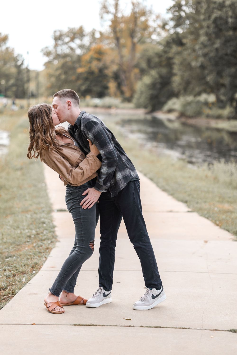 Romantic couple sharing a playful moment on a concrete path by the water.