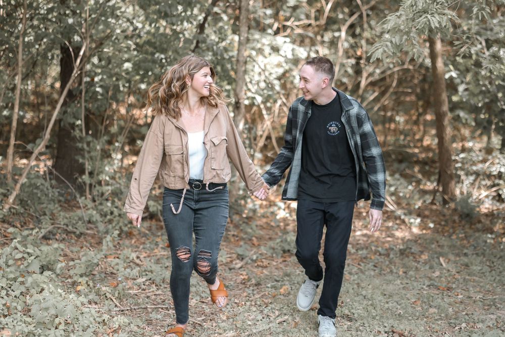 Couple walks through autumn woods sharing laughter along a nature path.