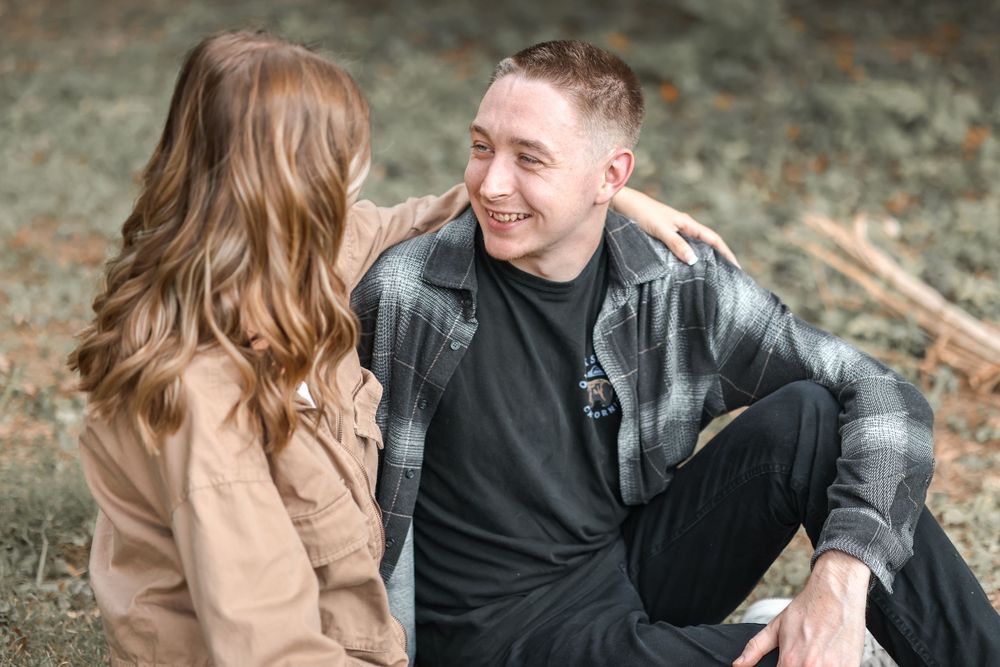A couple sitting outdoors sharing a candid laughing moment in casual fall attire.