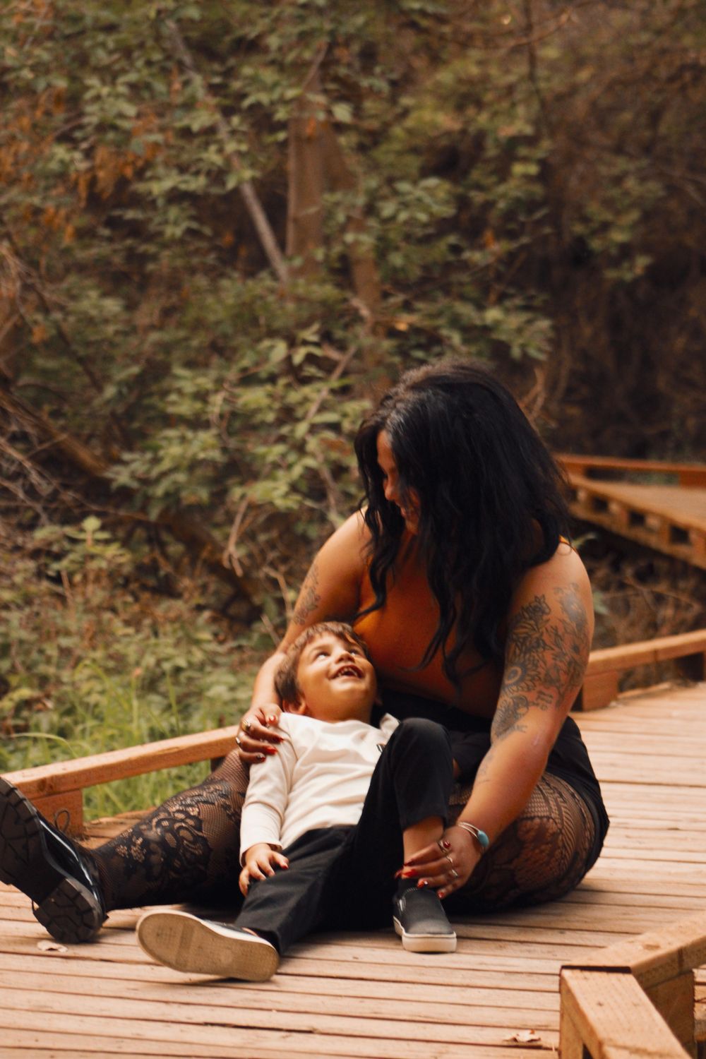 Adult and child sharing joyful moment while sitting on wooden boardwalk in nature.