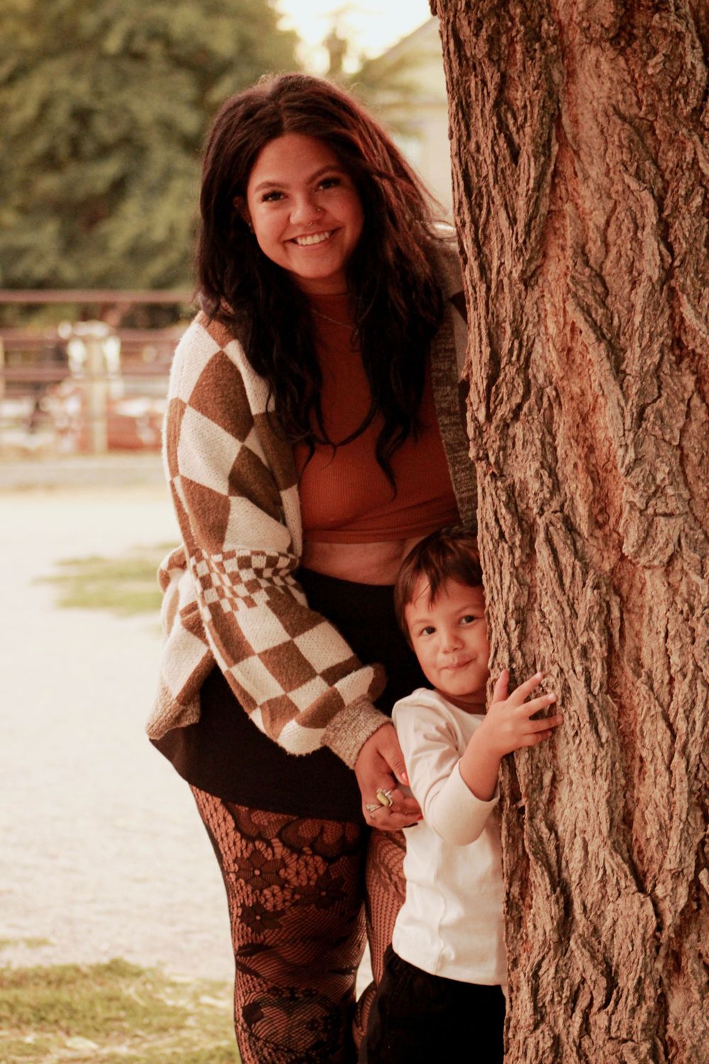 Adult and child pose by tree wearing matching autumn outfits in warm lighting.