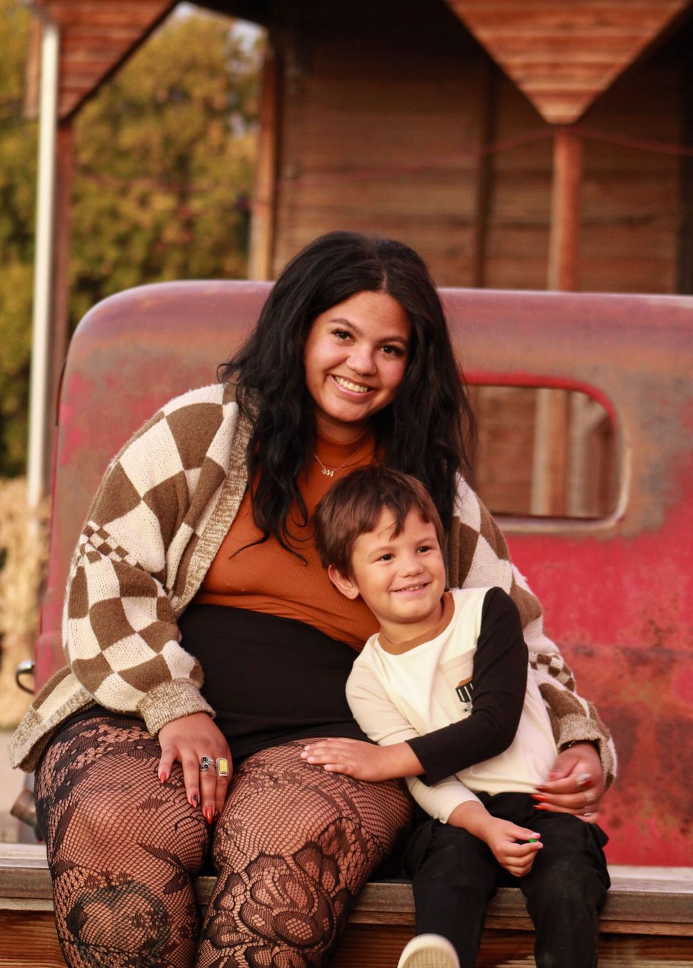 Adult and child sitting together on vintage red truck wearing checkered sweater.