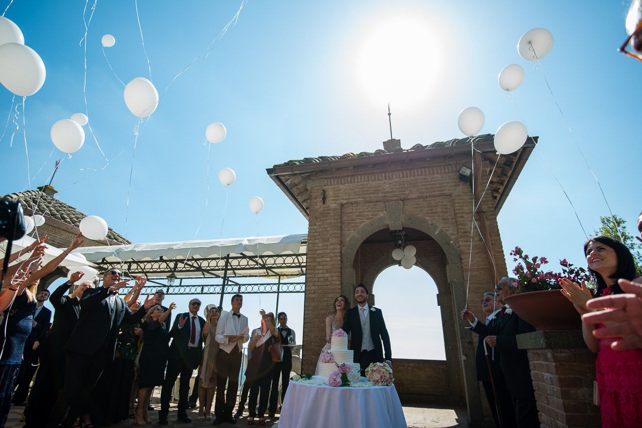 White balloons released into a bright blue sky during an outdoor wedding celebration.