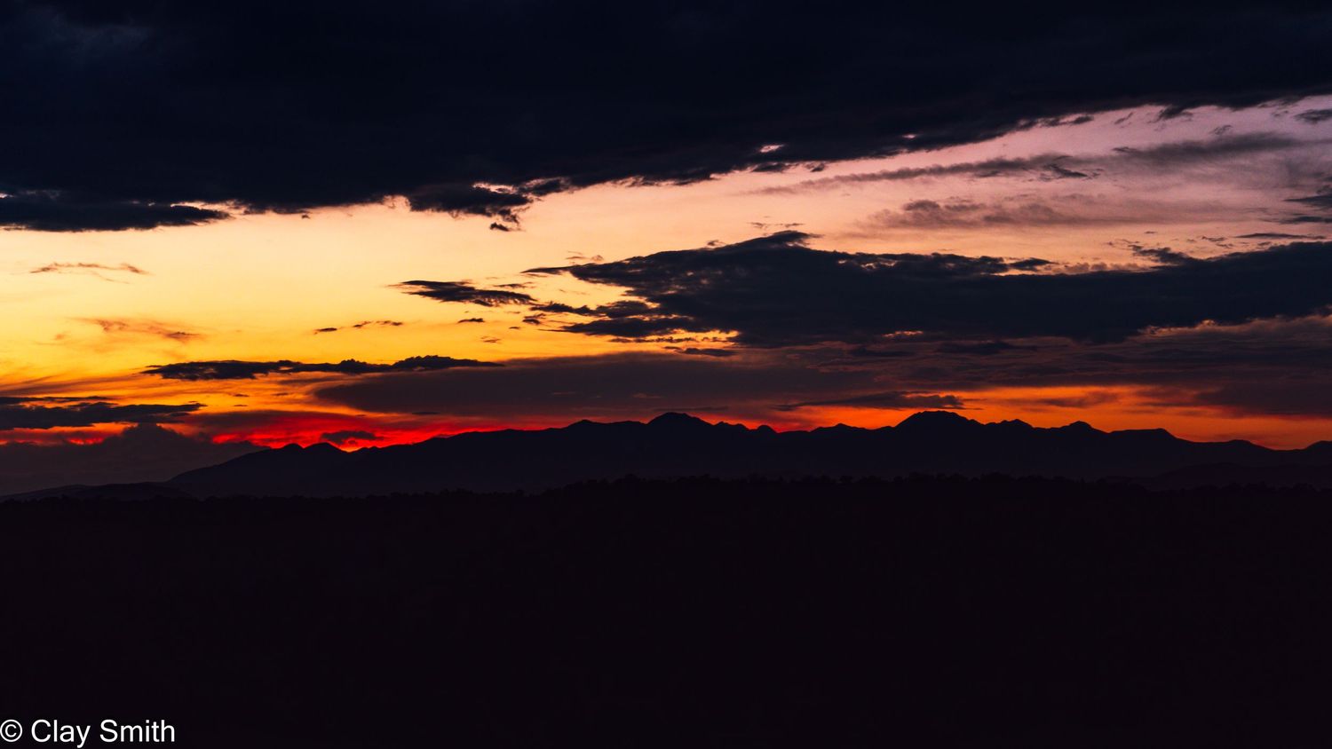 Vibrant orange sunset sky with dark silhouetted mountains against dramatic clouds during dusk.