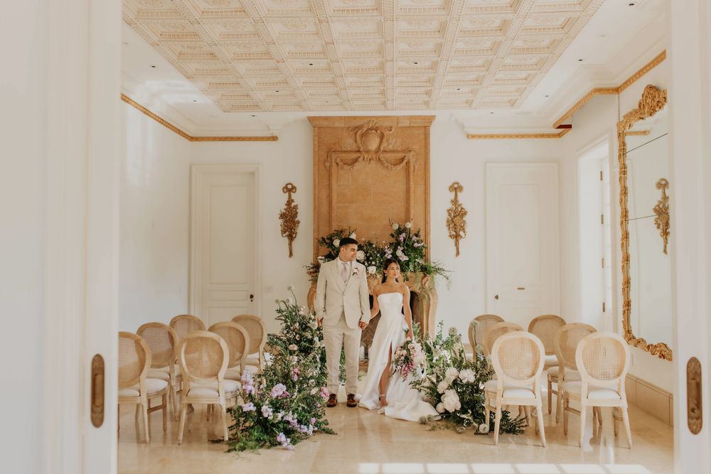 Elegant white wedding ceremony setup in a luxurious room with ornate details and floral arrangements.