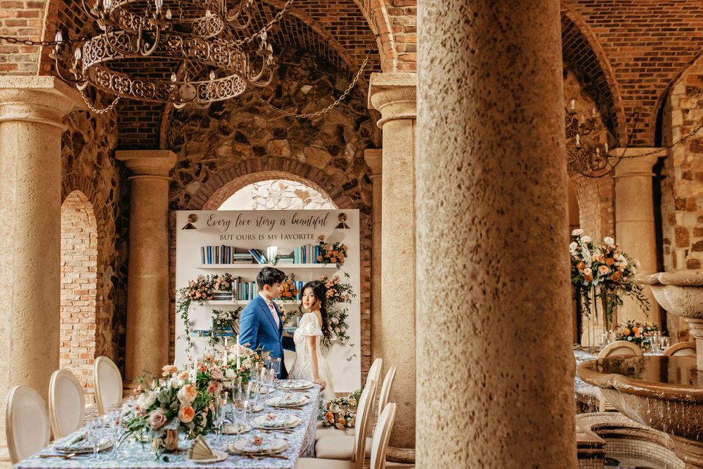 An elegant wedding reception table setup in a columned venue with chandeliers and floral arrangements.