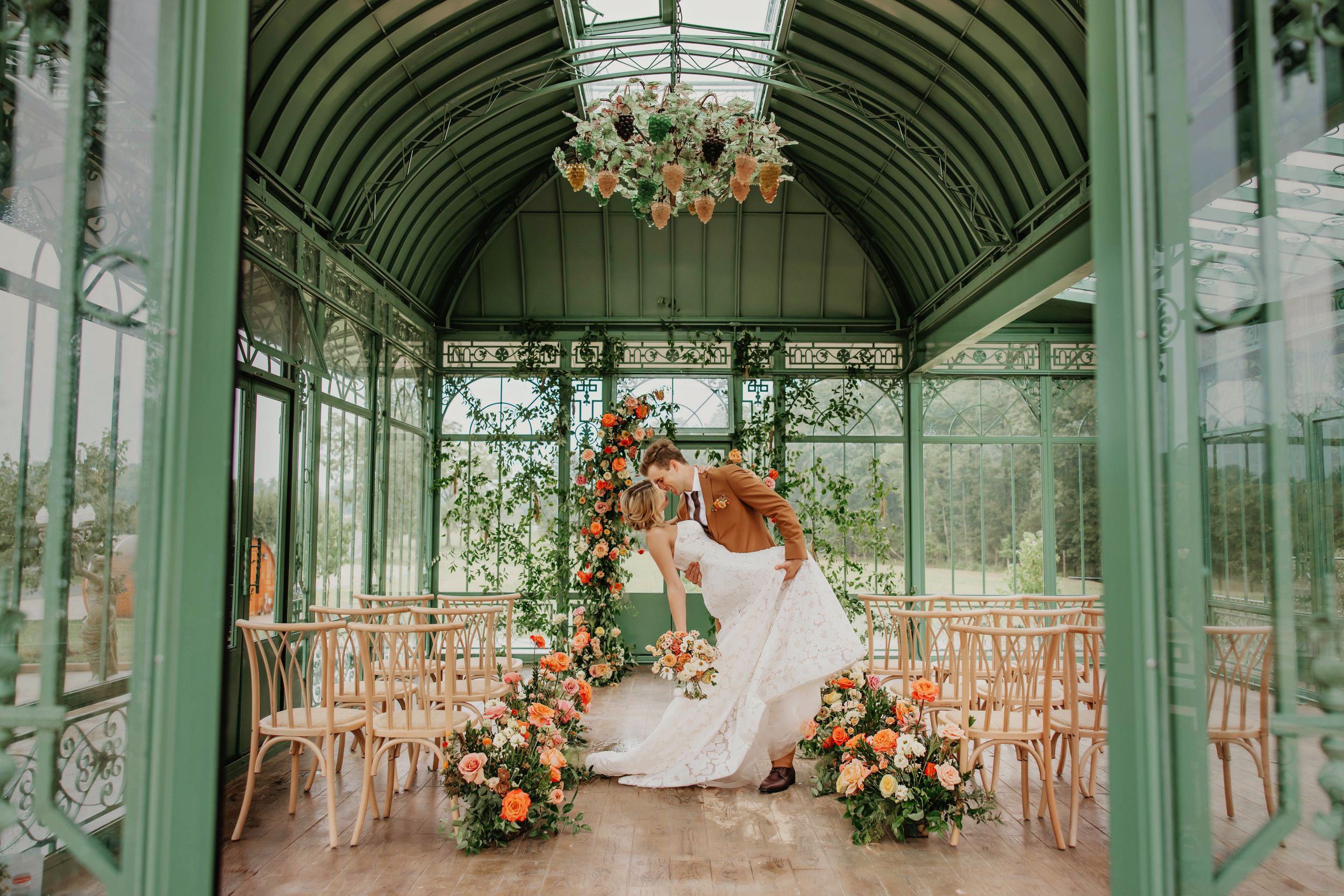 Elegant greenhouse wedding venue decorated with floral arrangements and vintage chairs.
