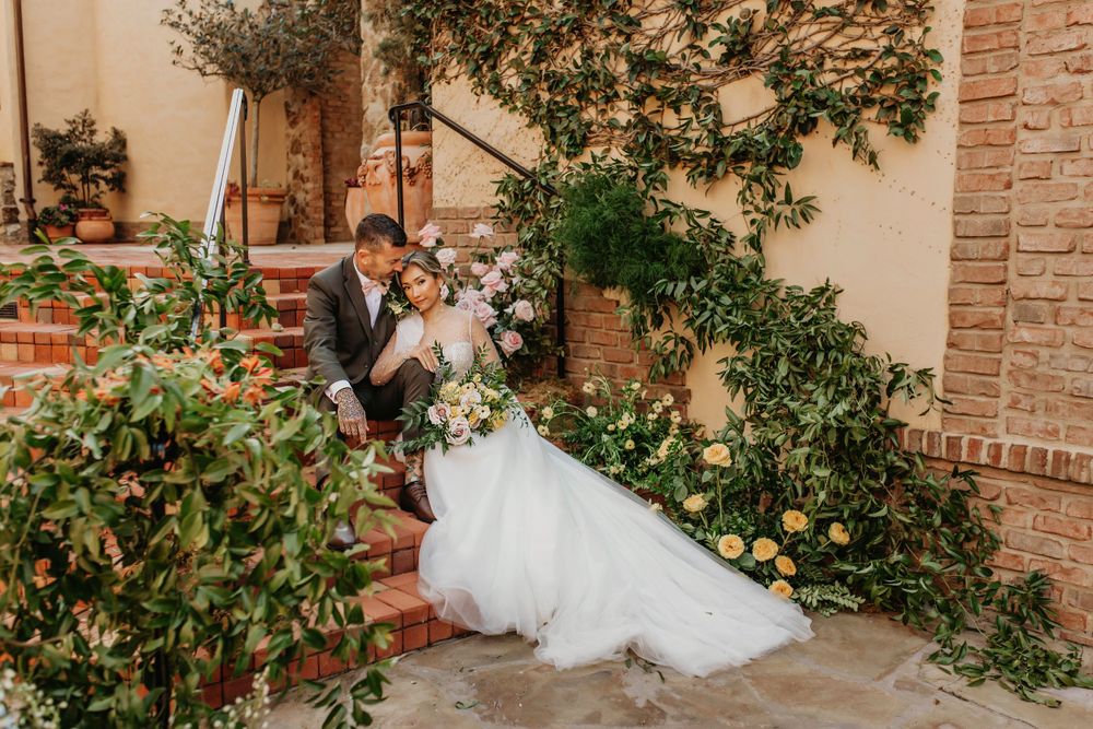 A romantic wedding couple shares an intimate moment on brick steps surrounded by gardens.