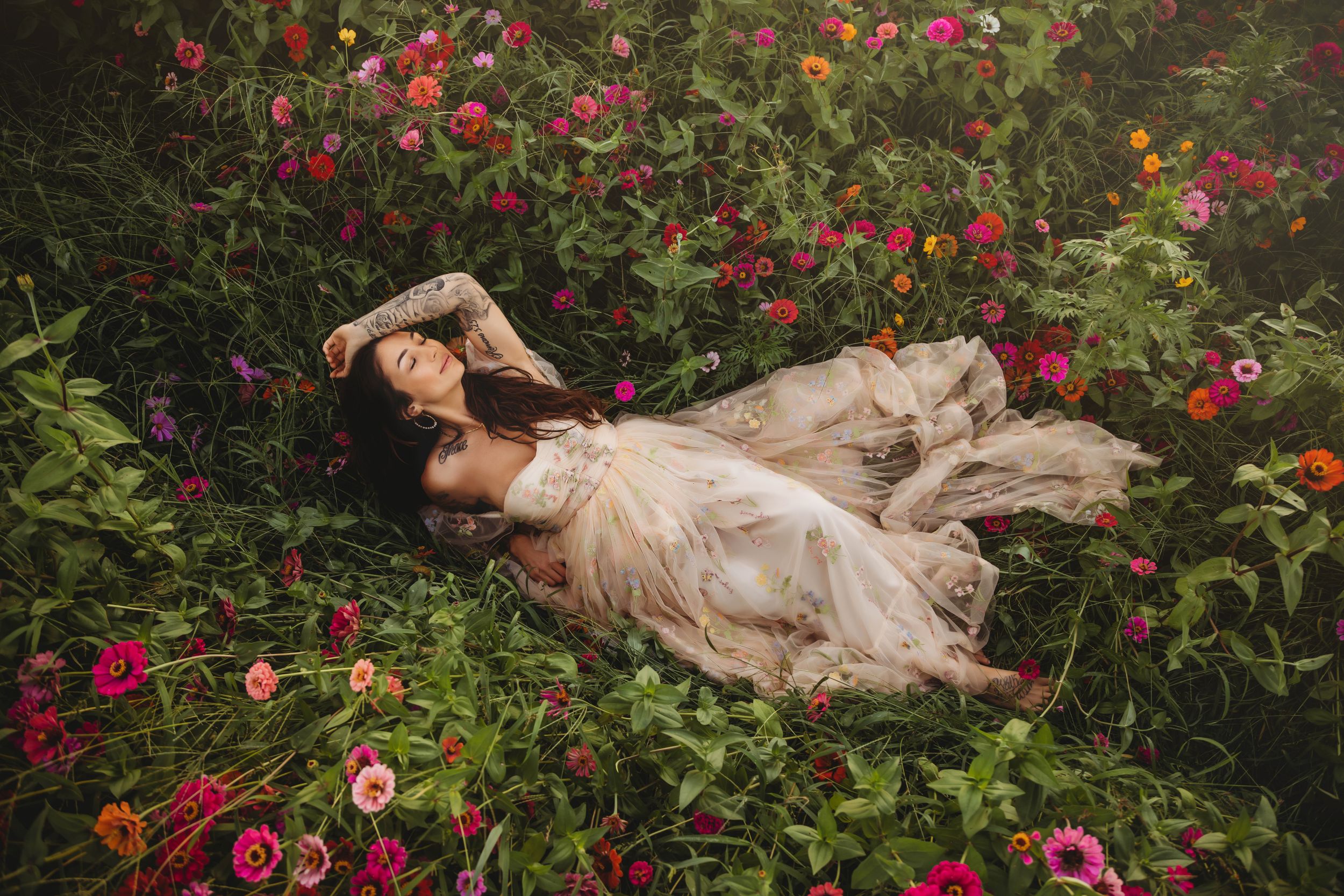 Person in flowing dress lies among blooming red roses in enchanted garden setting.