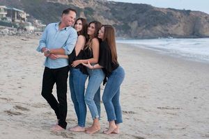 Legacy family photo on the beach with the three daughters adoring their father in Dana Point, California