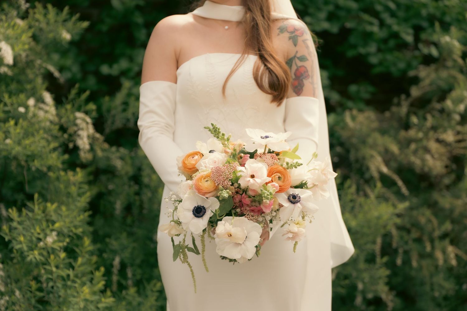A bride and her bridesmaids in floral dresses stand together on a vast lawn under cloudy skies.